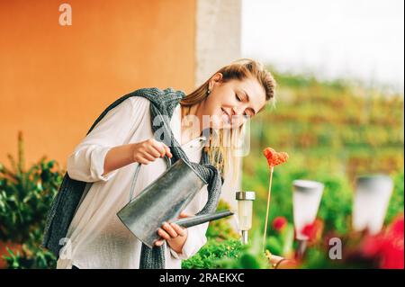 Portrait der schönen Frau Gießen grünen Pflanzen auf dem Balkon, kleinen gemütlichen Garten in der Wohnung Stockfoto