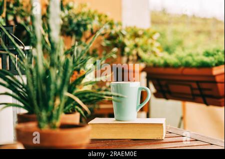 Gemütlicher Sommerbalkon mit vielen Topfpflanzen, einer Tasse Tee und einem alten Jahrbuch Stockfoto