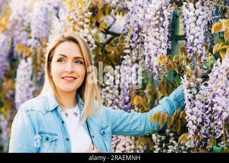 Frühlingsporträt einer eleganten jungen Frau mit Jeansshirt, die sich draußen im Wisteria-Garten aufstellt Stockfoto