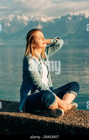 Außenporträt einer glücklichen jungen Frau, die sich am See an einem schönen sonnigen Tag mit friedlicher und harmonischer Stimmung entspannt Stockfoto