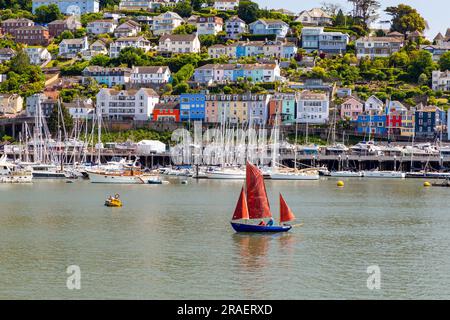 Farbenfrohe Aussicht auf Kingwear mit rotem Segelboot, verankerten Booten am Yachthafen und River Dart. Stockfoto