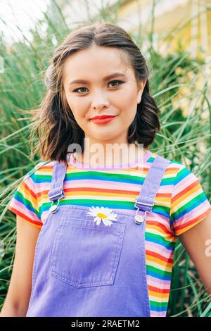 Außenporträt einer glücklichen jungen asiatischen Frau, die draußen posiert, ein farbenfrohes T-Shirt trägt Stockfoto