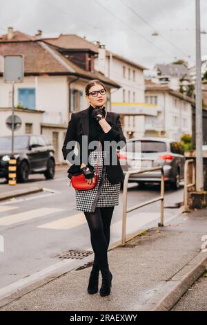 Outdoor-Modeporträt einer jungen, stilvollen Frau, die auf der Straße posiert, eine schwarze Jacke trägt und einen Karo-Rock trägt Stockfoto