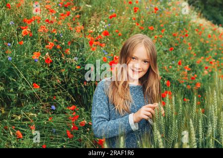 Außenporträt eines bezaubernden, kleinen blonden Mädchens mit 8-9 Jahren im Mohnfeld Stockfoto