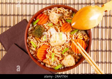 Gebratene Nudeln mit Gemüse in einer braunen Schüssel auf Holzhintergrund umrühren. Draufsicht. Stockfoto