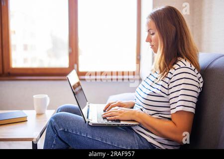 Junge Frau mit einem Laptop und einer Tasse Kaffee auf dem Tisch zu Hause. Stockfoto