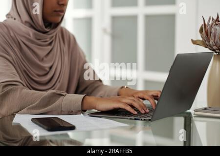 Zugeschnittene Aufnahme einer jungen Geschäftsfrau, die auf der Laptop-Tastatur per Hidschab tippt, während sie im Home Office am Arbeitsplatz sitzt und die Arbeit organisiert Stockfoto