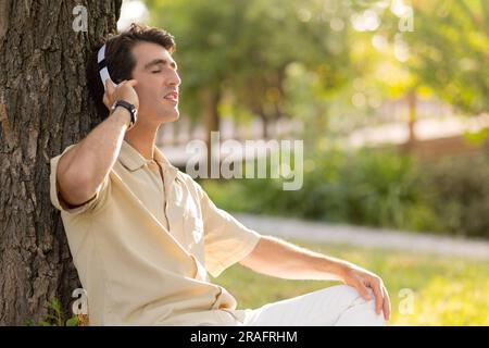 Fröhlicher junger weißer Mann, der im Park Musik hört Stockfoto