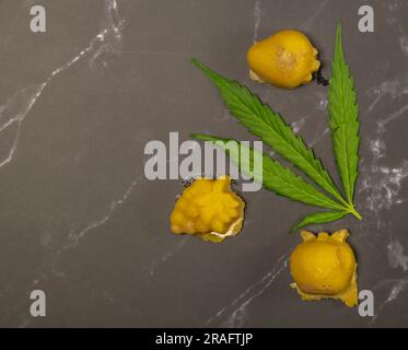 Ein kleines Stück Marihuana-Butter am heißen Tag auf einem schwarzen Marmortisch mit grünem frischem Blatt Stockfoto