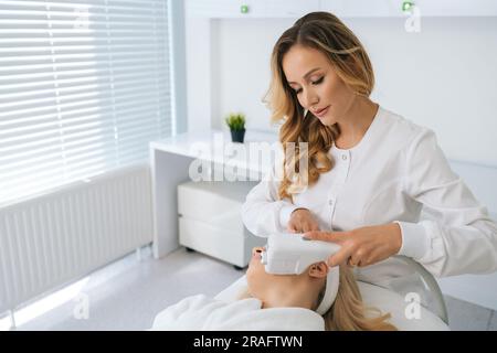 Blonde junge Frau, die sich einer Gesichtshobelebungsbehandlung mit Radiofrequenz unterzieht. Gesichtspflege, Anti-Aging-Gesichtsverjüngung. Stockfoto