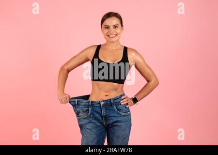 Eine Fröhliche, Sportliche Frau Mit Übergroßen Jeans, Die Das Ergebnis Der Gewichtsreduktion Demonstriert Stockfoto