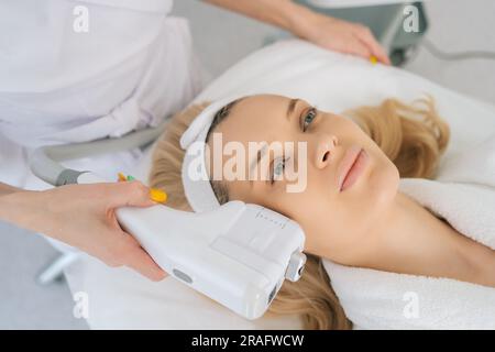 Nahaufnahme von oben bei einer jungen Frau unter HUFU-Therapie mit hochintensiver Ultraschallbehandlung im Gesicht. Kosmetologe, der nichtchirurgisches Kosmetikplasma macht Stockfoto