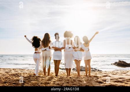 Brautteam. Rückblick auf eine Gruppe junger, vielfältiger Frauen, die sich am Meer posieren und umarmen. Hühnerfeier Stockfoto