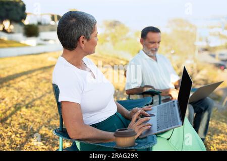 Ältere Freiberufler, Ehepartner, Die Laptops Nutzen, Sitzen Draußen Im Summer Park Stockfoto