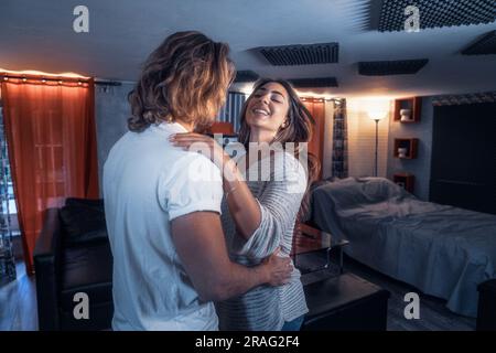 Ein Paar im Haus, das im Wohnzimmer tanzt und Spaß hat, lächelt und lautstark - Gelbes und blaues Licht. Liebhaber haben beim Flirten den Ball gedreht Stockfoto