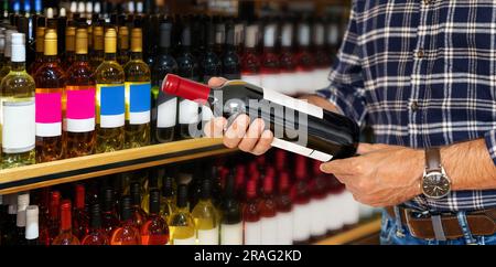 Kunde im Geschäft hält eine Flasche Wein in der Hand und liest Informationen über den Wein auf dem Etikett. Stockfoto