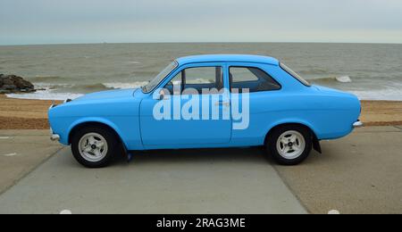 Der klassische hellblaue Ford Escort Motor Car parkt am Ufer der Promenade und im Hintergrund am Meer. Stockfoto