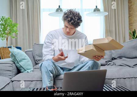 Junger Mann packt einen Online-Kauf aus, mit Box mit neuem Smartphone Stockfoto