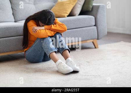 Aufgewühlte junge Brünette, die auf dem Boden saß und weinte Stockfoto
