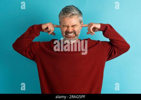 Gereizter, grauhaariger reifer Mann, der mit Fingern Ohren verstopft Stockfoto