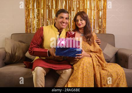 Ein glücklicher Indianer bringt seiner Frau in Saree ein wunderbares Geschenk. Beide tragen indische ethnische Kleidung auf Diwali und feiern das Festival. Stockfoto