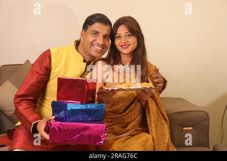 Glücklicher Indianer bringt Geschenk für seine wunderschöne Frau in Saree.Diwali Festival zu diesem Anlass .Frau hält ein gesundes Trockenobsttablett in der Hand Stockfoto