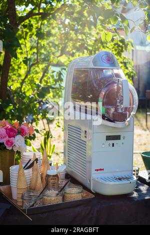 Tallinn, Estland - 30. Juni 2023: Weicheismaschine Ugolini mit Waffelkonusbechern und Streuseln bei einer Sommerparty im Garten. Stockfoto