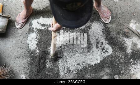 Asiatischer Arbeiter, der Hacke zum Mischen von Zementkraft und Sand verwendet Stockfoto