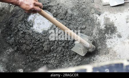 Asiatischer Arbeiter, der Hacke zum Mischen von Zementkraft und Sand verwendet Stockfoto