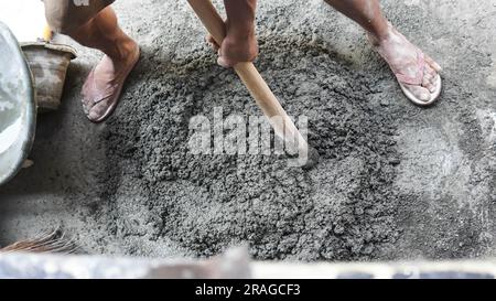 Asiatischer Arbeiter, der Hacke zum Mischen von Zementkraft und Sand verwendet Stockfoto