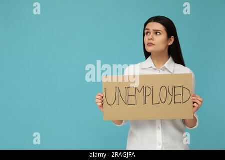 Unglückliche Frau, die ein Schild mit dem Wort arbeitslos auf hellblauem Hintergrund hält. Platz für Text Stockfoto