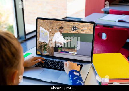 Vielfältiges Schulmädchen mit männlichem Lehrer, der während eines Laptop-Videogesprächs Unterricht hat Stockfoto