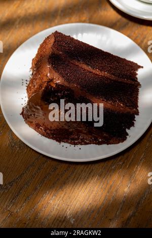 Schokoladenkuchenschnitt ist ein großes Stück mit einer Tasse Kaffee auf der Rückseite Stockfoto