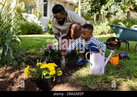 afroamerikanischer Vater, der Sohn beim Graben von Erde unterstützt, um Blumen auf dem Feld im Garten zu Pflanzen Stockfoto