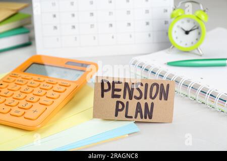 Karte mit den Worten Pensionsplan, Taschenrechner und Briefpapier auf weißem Bürotisch, Nahaufnahme Stockfoto