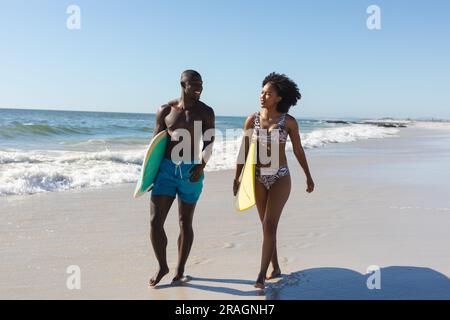 Glückliches, fittes afroamerikanisches Paar mit Surfbrettern am Strand am Meer Stockfoto