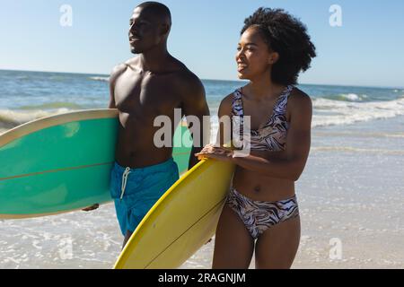 Glückliches, fittes afroamerikanisches Paar mit Surfbrettern am Strand am Meer Stockfoto