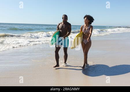 Glückliches, fittes afroamerikanisches Paar mit Surfbrettern am Strand am Meer Stockfoto