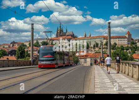 Die rote Straßenbahn überquert die Manes-Brücke mit der Prager Burg im Hintergrund Stockfoto