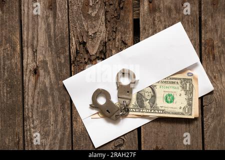 amerikanische Dollar liegen auf einem alten Holztisch neben Handschellen, Finanzen und Korruption Stockfoto