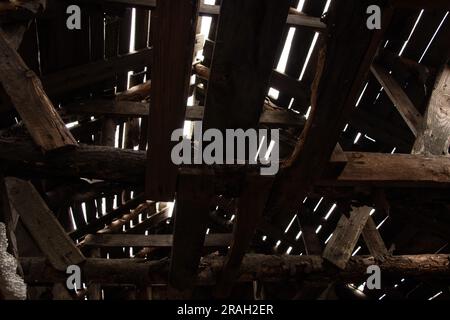 Ein Dachboden aus Holzplanken und Balken mit Rissen, aus denen das Sonnenlicht austritt, ein altes zerstörtes Holzdach Stockfoto