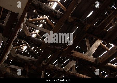 Ein Dachboden aus Holzplanken und Balken mit Rissen, aus denen das Sonnenlicht austritt, ein altes zerstörtes Holzdach Stockfoto