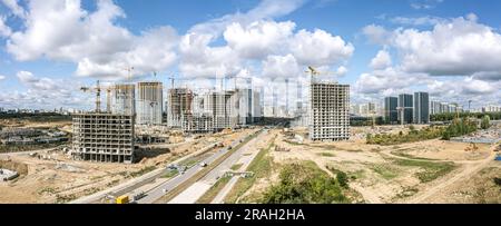 Hochhäuser im Bau und funktionierende Kräne vor blauem bewölktem Himmel. Panoramablick aus der Vogelperspektive. Stockfoto