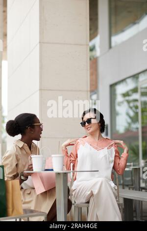 Stilvolle junge Frau, die am Kaffeetisch sitzt und über Einkäufe diskutiert Stockfoto