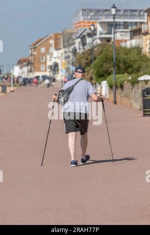 Ein alter Mann, der an einer Seside Promenade mit zwei Gehstöcken spaziert Stockfoto