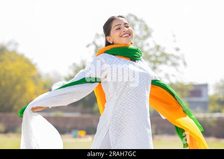 Porträt einer glücklichen jungen indischen Frau, die traditionelle weiße Kurta und dreifarbige Duppata trägt, die im Park laufen. Wir feiern den Unabhängigkeitstag oder die Republik da Stockfoto