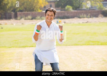 Portrait eines glücklichen, gutaussehenden jungen indianers, der traditionelle weiße Kurta trägt und im Park steht. Fans jubeln das Team an, feiern den Unabhängigkeitstag oder R Stockfoto