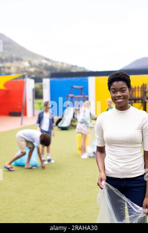 Vertikales Porträt einer glücklichen afroamerikanischen Lehrerin, die im Schulhof recycelt, Kopierraum. Bildung, Inklusivität, Grundschule und Lernen Stockfoto