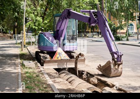 Bohrstraße für große Presslufthammer. Schwere Maschinen zerkleinern Asphalt für die Reparatur von Regenwasserabflüssen. Hydraulikbagger läuft im Wasser. Reparatur und Erweiterung Stockfoto