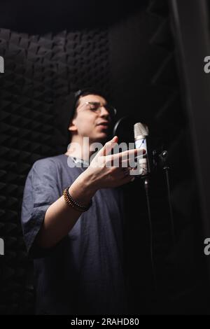 Mann singt in Mikrofon, professionelles Aufnahmestudio, Kopfhörer. Schwarze weiche Wände, Schalldämmung. Der Sänger nimmt sein Lied auf. Modern Stockfoto